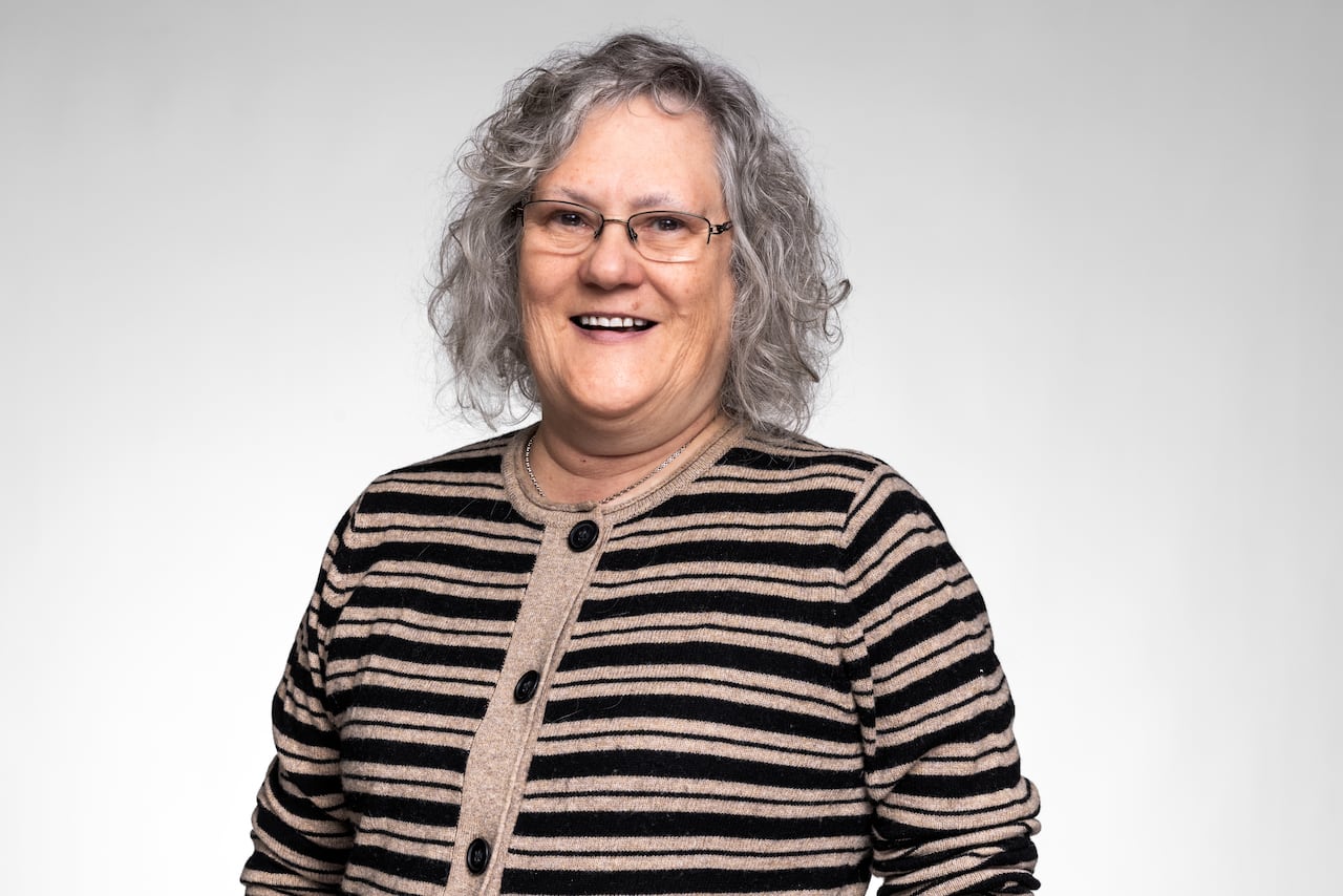 A smiling woman with curly gray hair and a striped sweater against a white backdrop