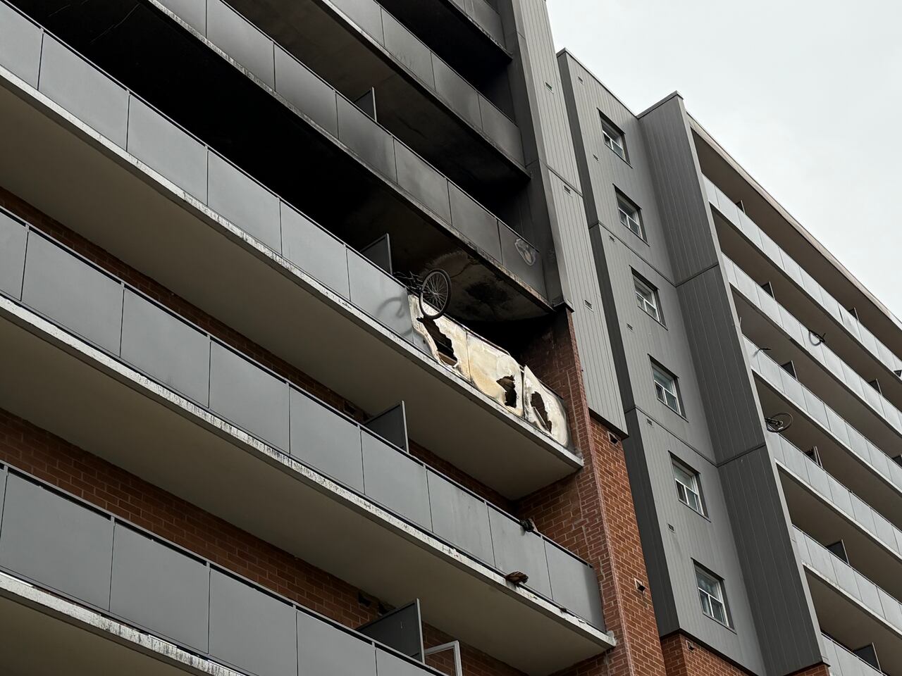 One balcony of a building with black smoke damage around its edges and glass broken out of the balcony