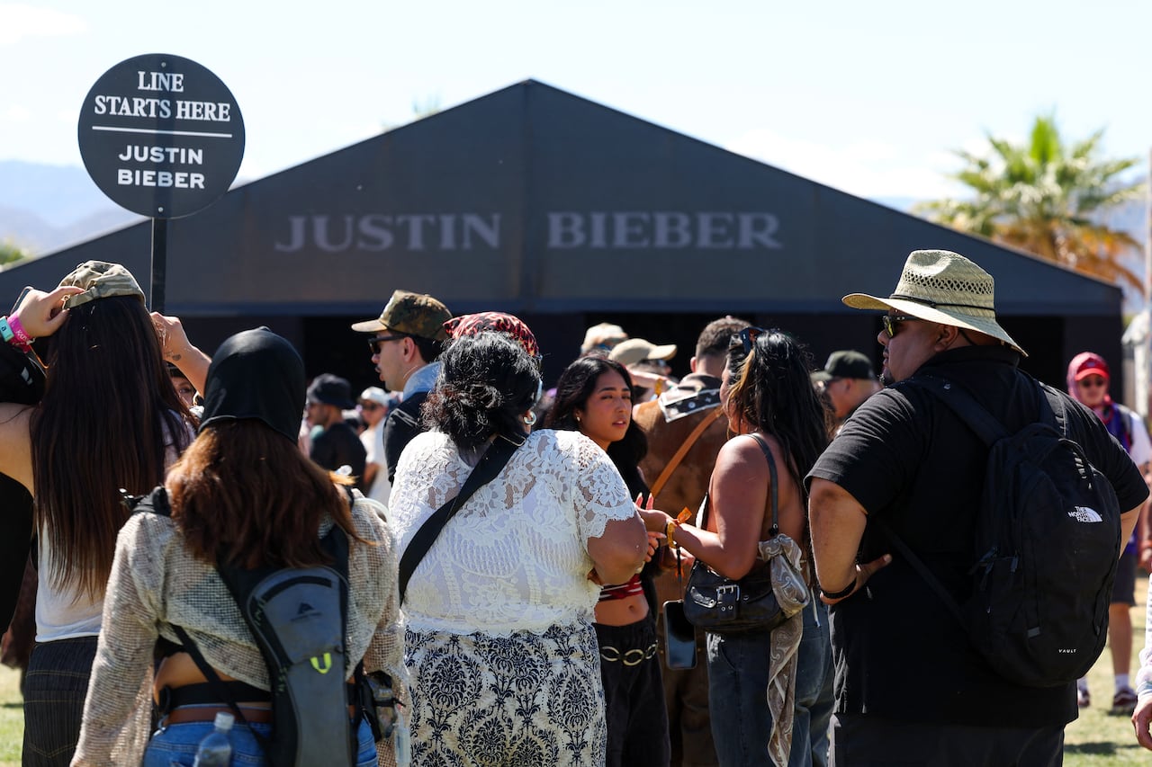 People line up outside a large tent that says Justin Bieber on it.