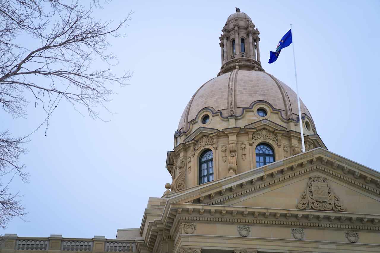 A blue flag flies on top of a large sable-coloured stone building with a large dome.