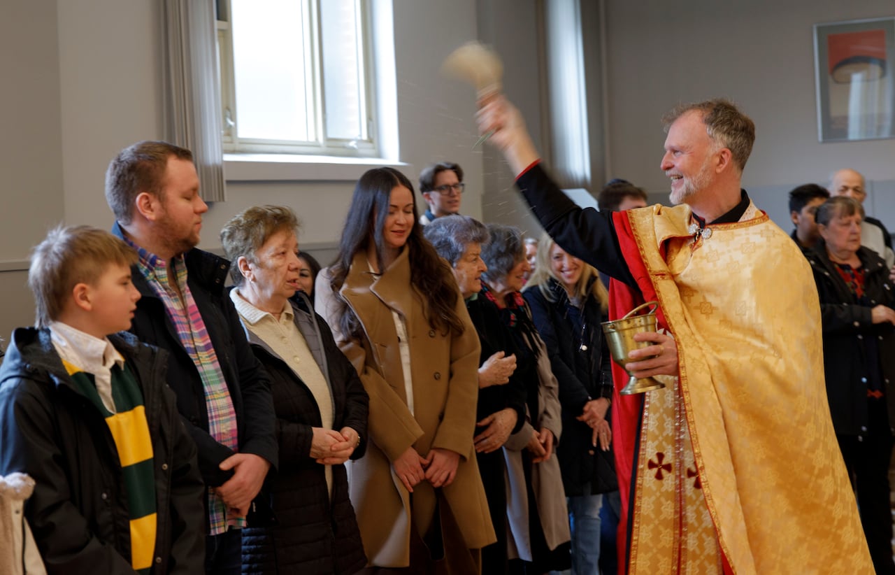 A father sprinkling parishioners with holy water from a brush. 