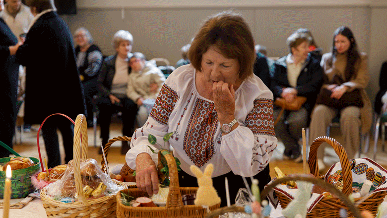 A woman at a food basket filled table looking over a basket, and a closeup of the food baskets filled with bread, eggs, treats, sausages and candles.