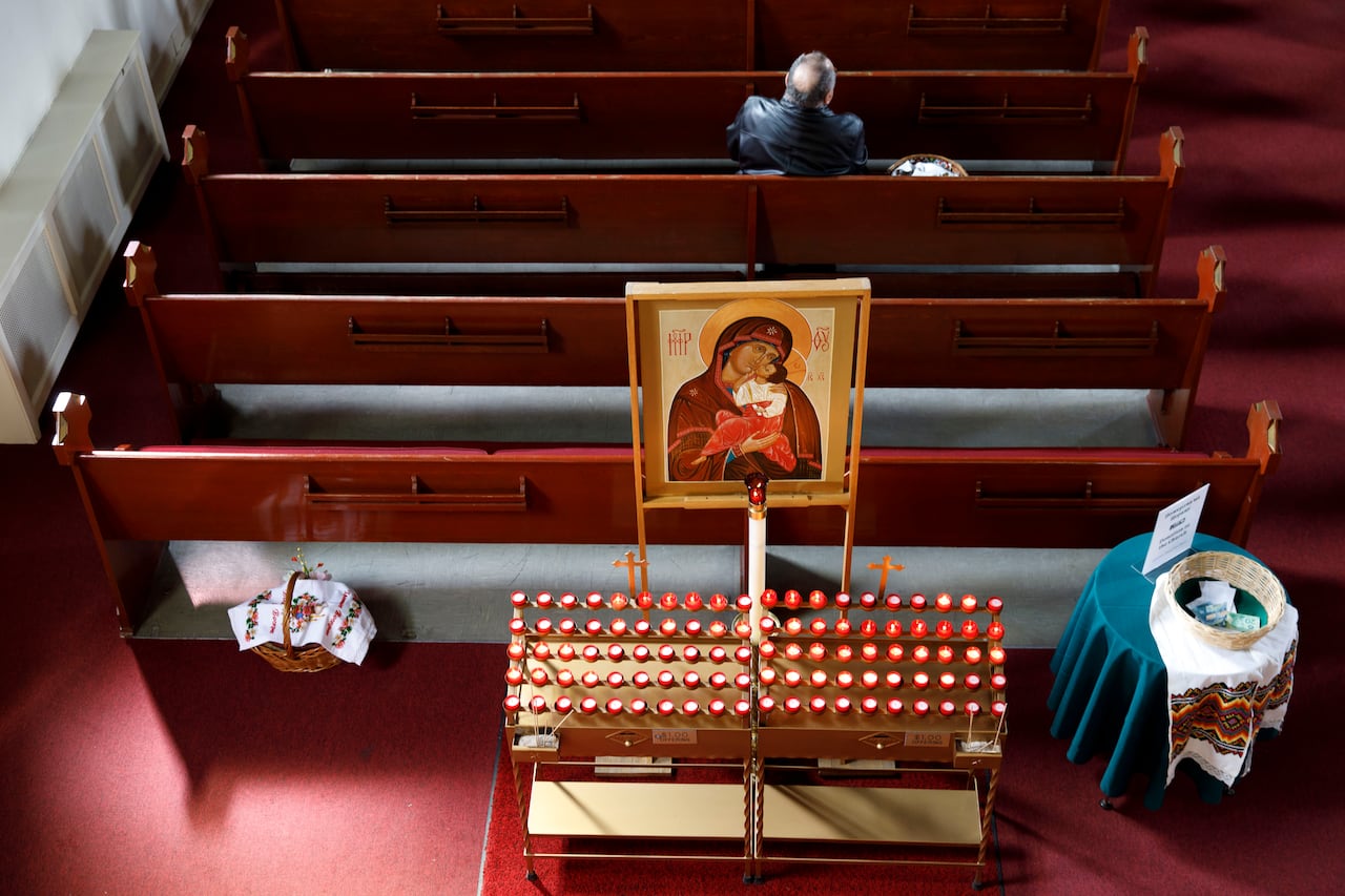 A bird's-eye view of church pews, with a man sitting and candles lit in front of a poster of Mary and baby Christ.