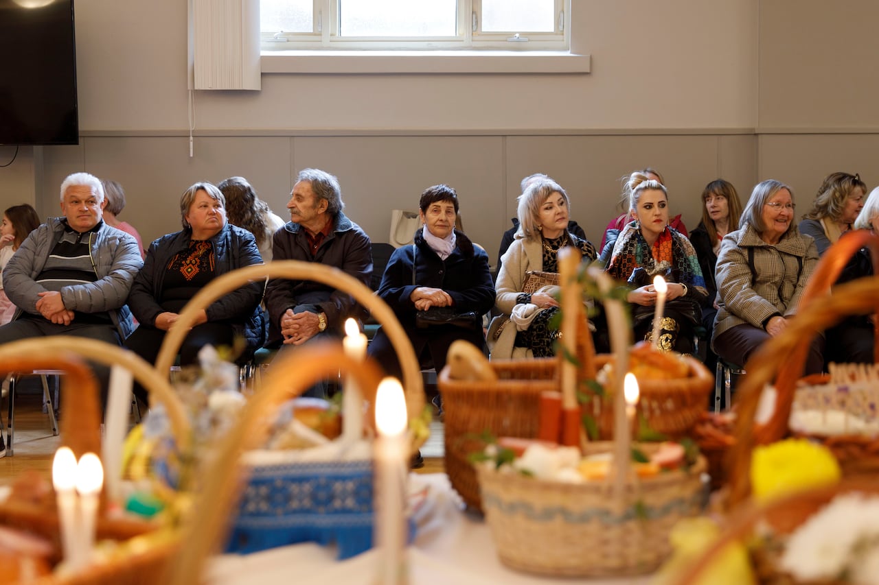 People sitting in chairs in their winter clothes in front of a table with baskets of food.
