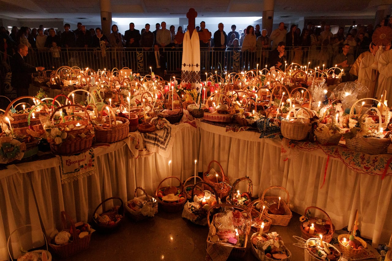 Food baskets fill tables laid together in an X-shape; they're each lit with a candle as churchgoers stand in the back of a room.