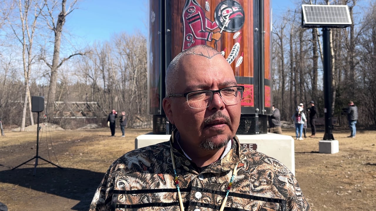 A man with glasses stands in front of a cedar pillar on a sunny day. 