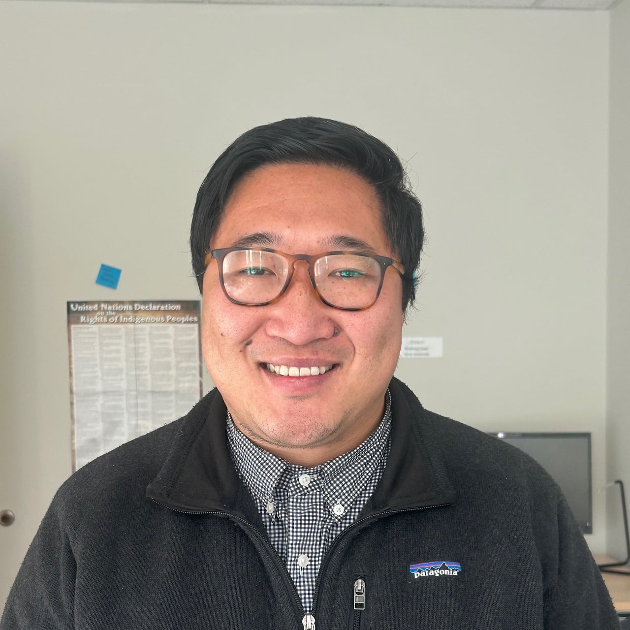 Portrait of a smiling man wearing glasses in an office setting. 