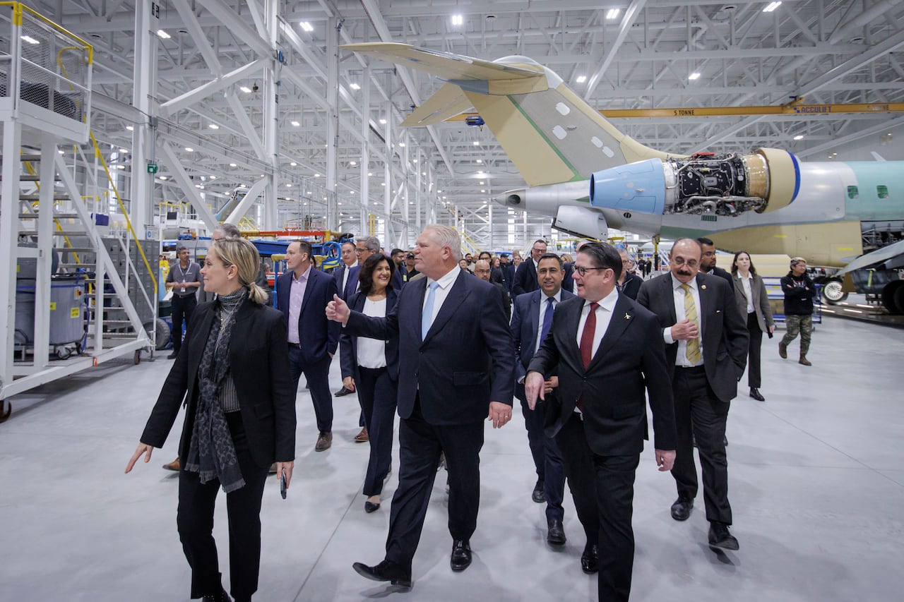 A group of people walking in front of a plane that's under construction.