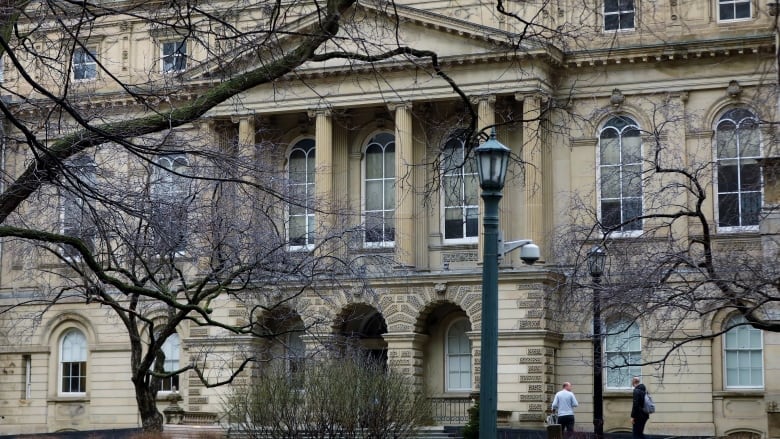 A grey stone building with columns and trees out front 