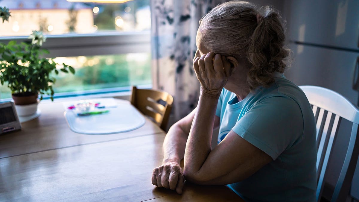 Sad elderly woman looking out a home window