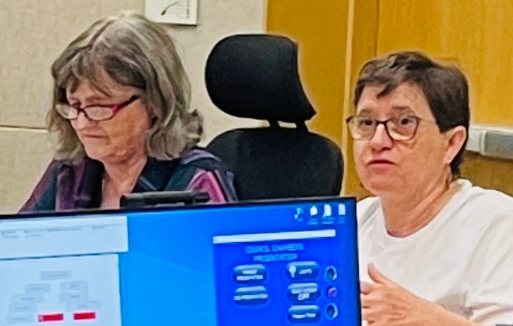 Two women, one of whom has long hair and another short hair, are seen in council chambers.