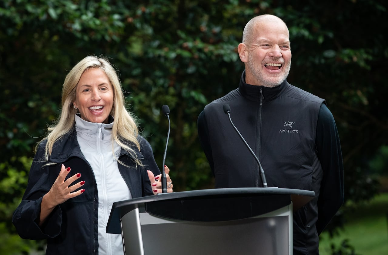 A blond woman and a bald man laugh at an outdoor podium.