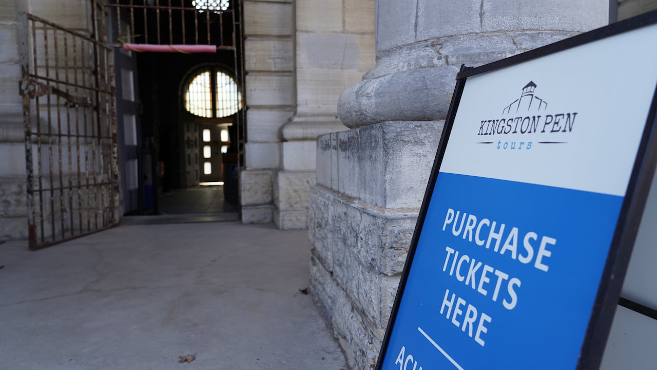 A sign for "Kingston Pen Tours" stands outside of an open prison door.