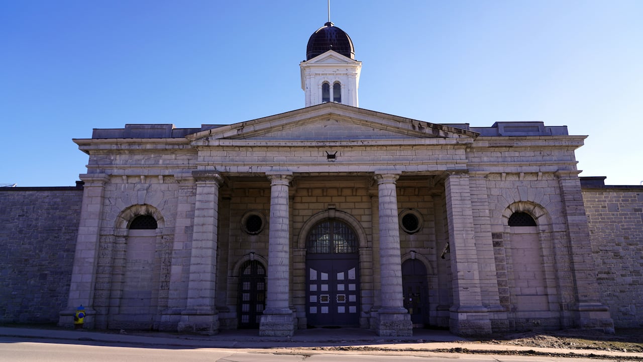 High stone walls and pillars are shown in front of tall wooden gates with bars on them.