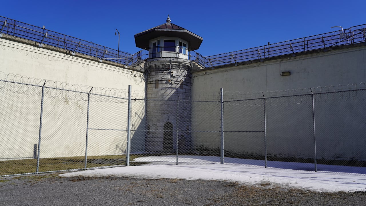 A guard tower is flanked by high concrete walls and barbed wire.