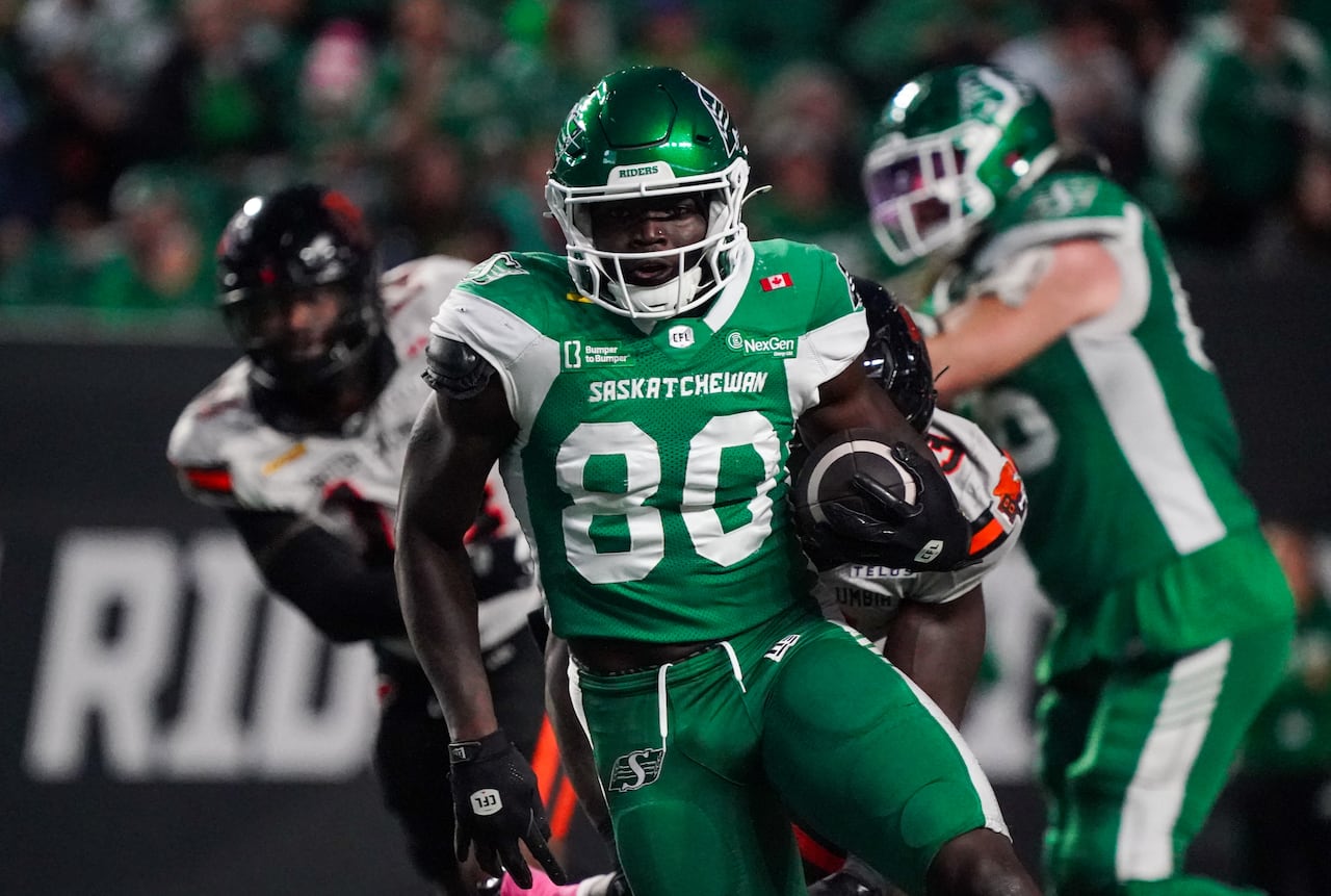 A football player cradles a football while running during a game in a stadium at night.