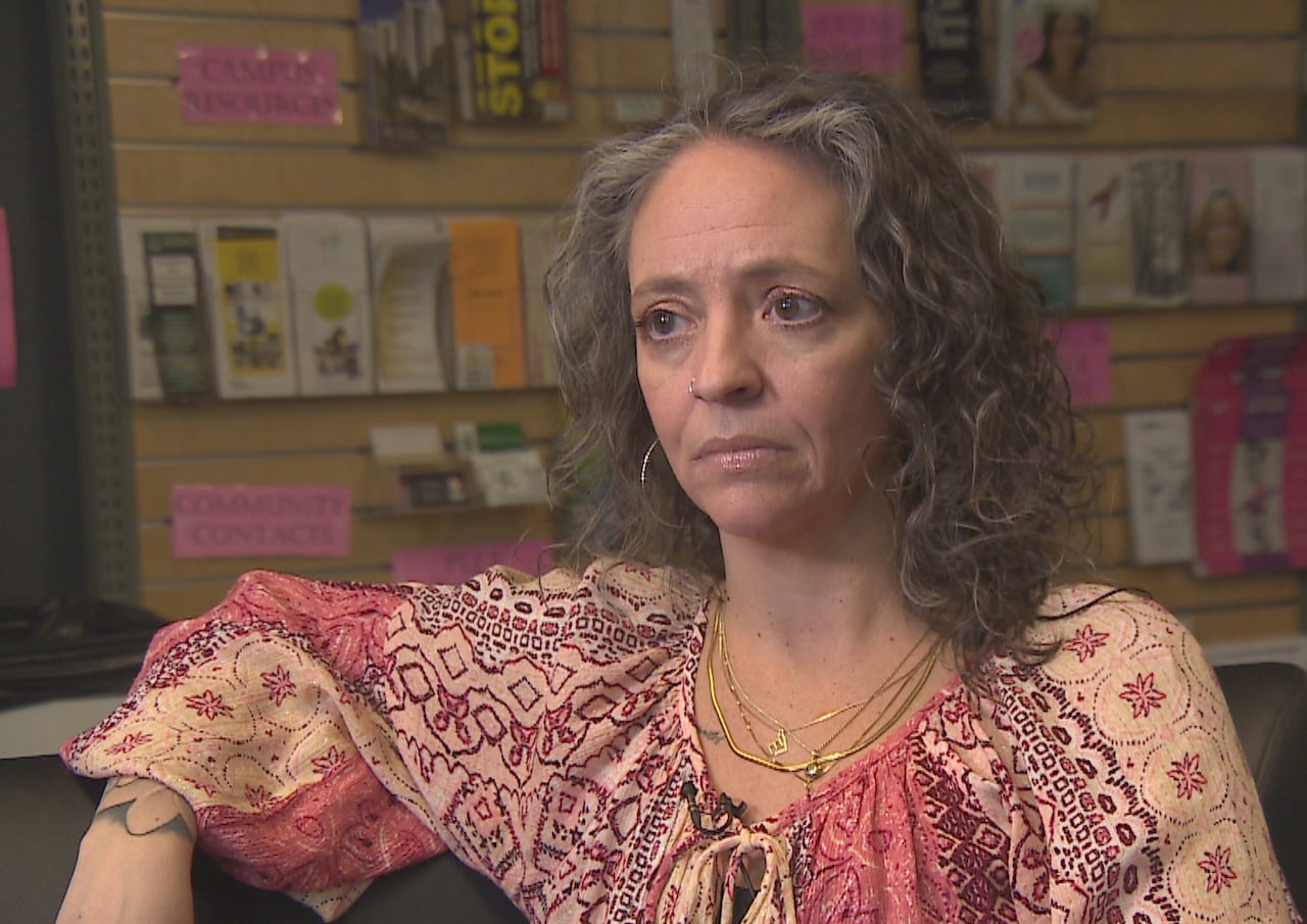 A woman with curly hair sits in front of a wall lined with brochures.