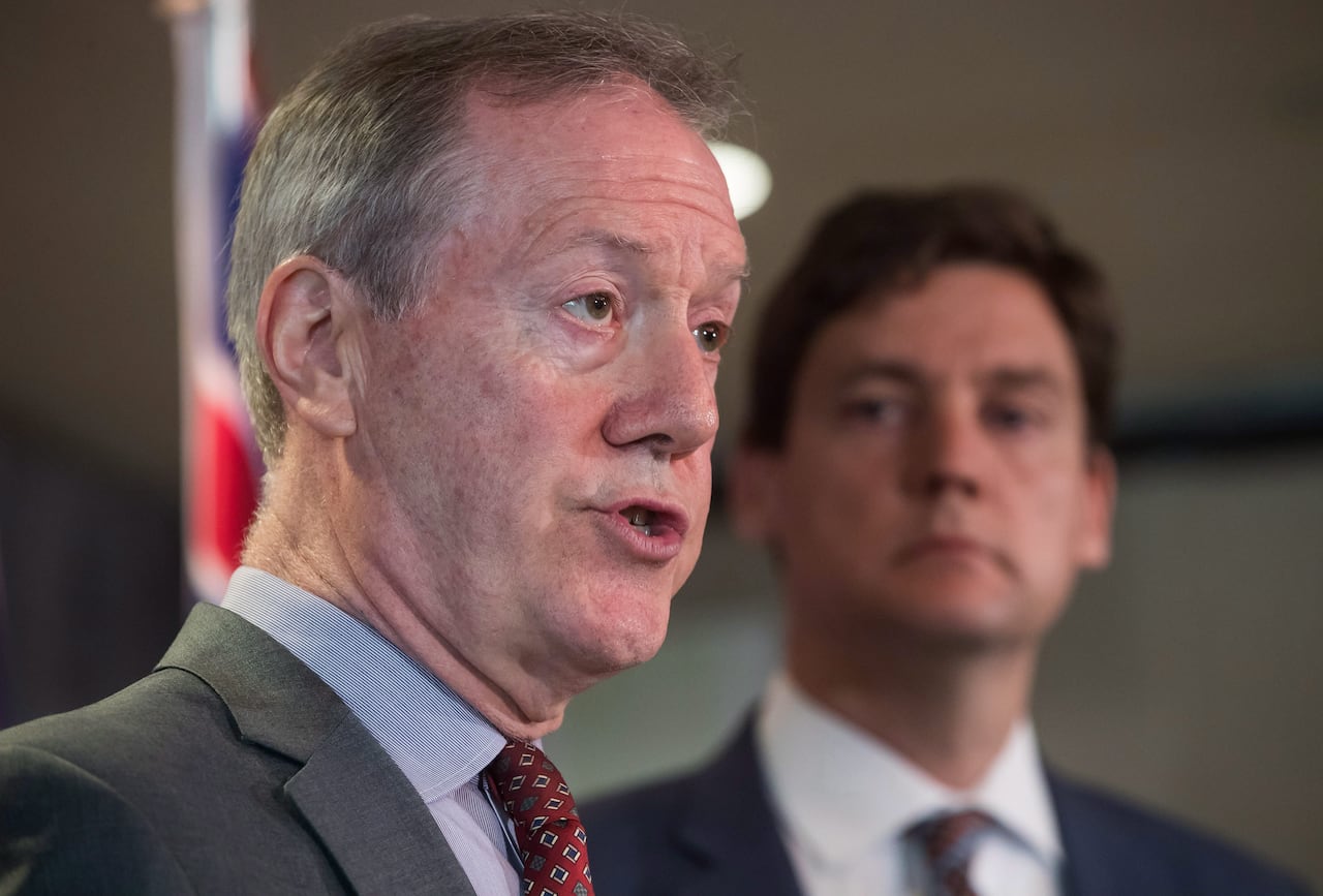 Two men in suits, one in focus in front and one out of focus in the background.