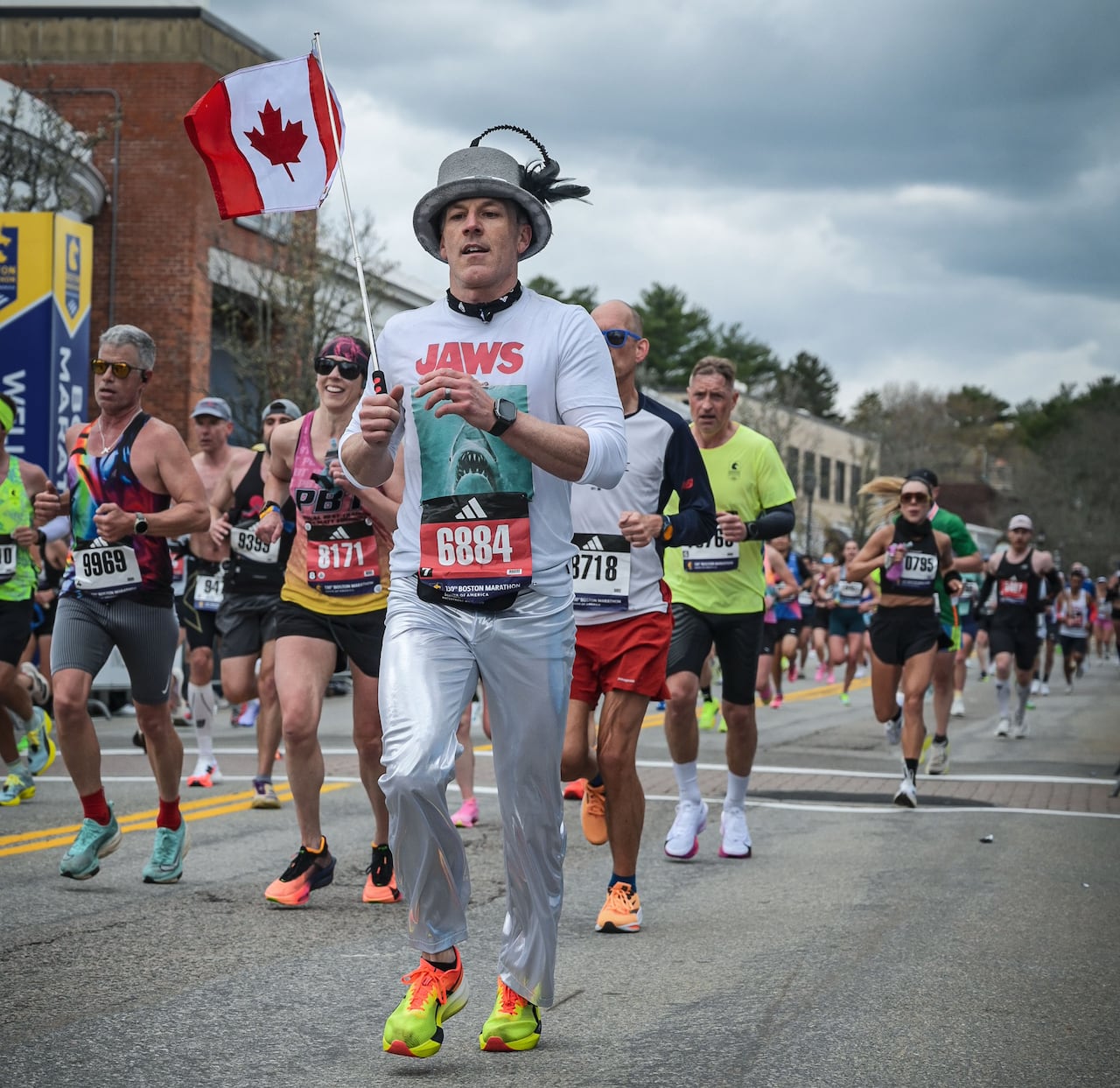 A man in silver pants and a t-shrt that says Jaws runs while holding a  canadian flag