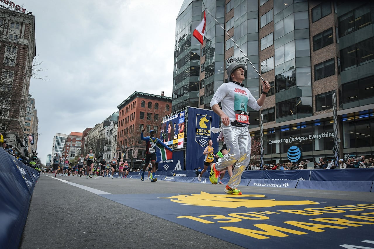 A man in silver pants runs on a race course holding a canadian flag