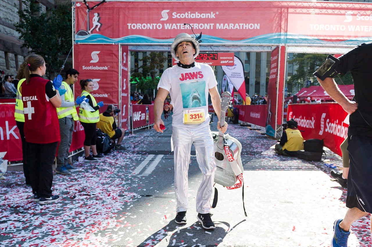 A runner dressed in silver pants, a jaws tshirt, a silver hat, carrying a guitar