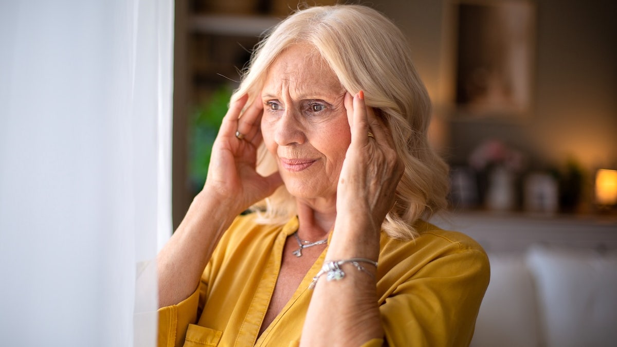 Senior woman holding her head with hands, sitting at home