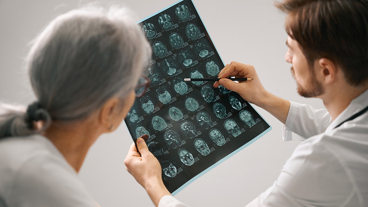 Doctor holding an MRI scan of a brain while consulting an elderly woman