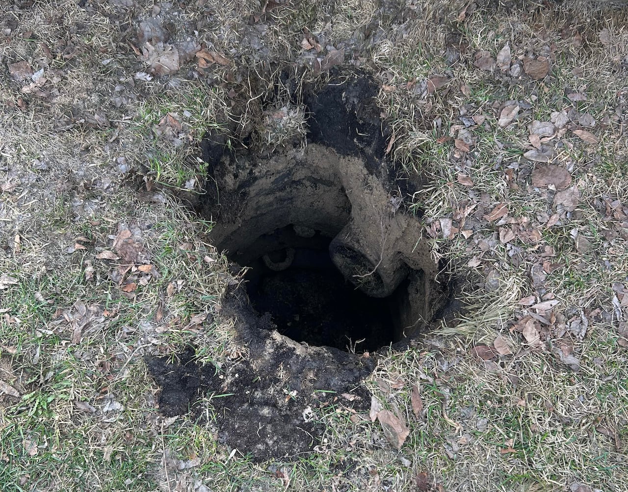 Looking down into a large hole in a grassy boulevard.
