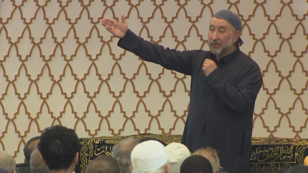 A man in a stands infront of a crowd in a mosque.