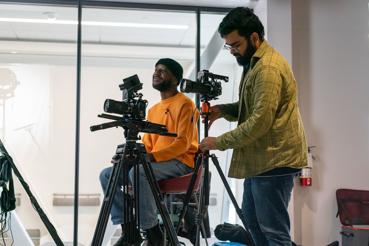 Two people stand behind cameras on set.