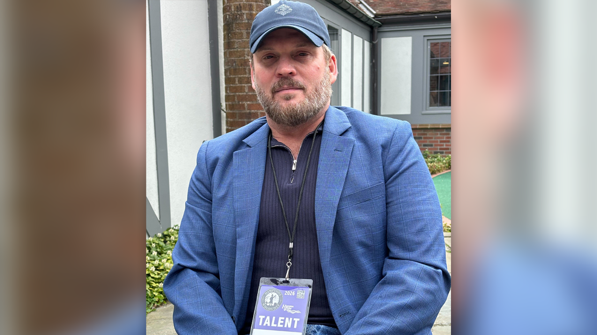 Alex Baber wears a blue sportscoat, ballcap and black shirt in an interview at the East Hampton Library's courtyard