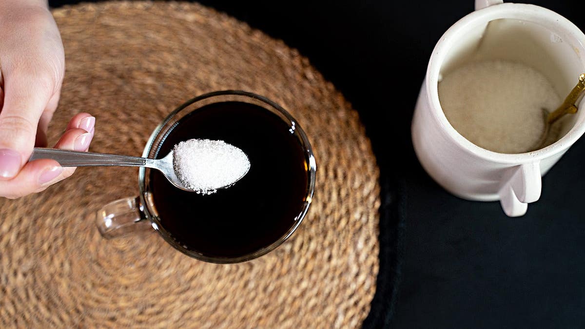 Spoonful of sweetener being poured in black coffee, seen from overhead.