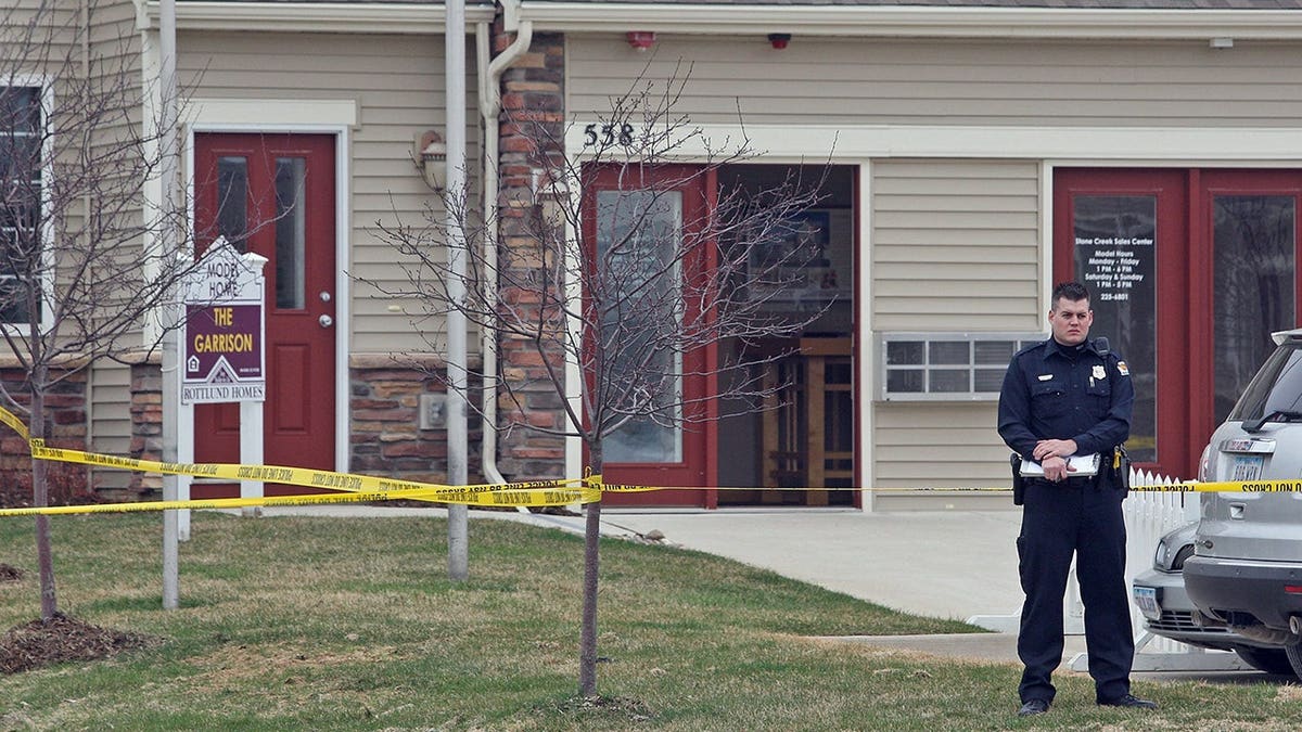West Des Moines police officer standing near crime scene tape at outdoor site
