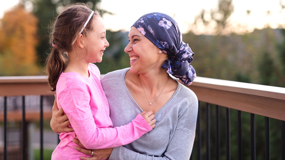 A young mother wearing a head scarf hugs and smiles at her daughter