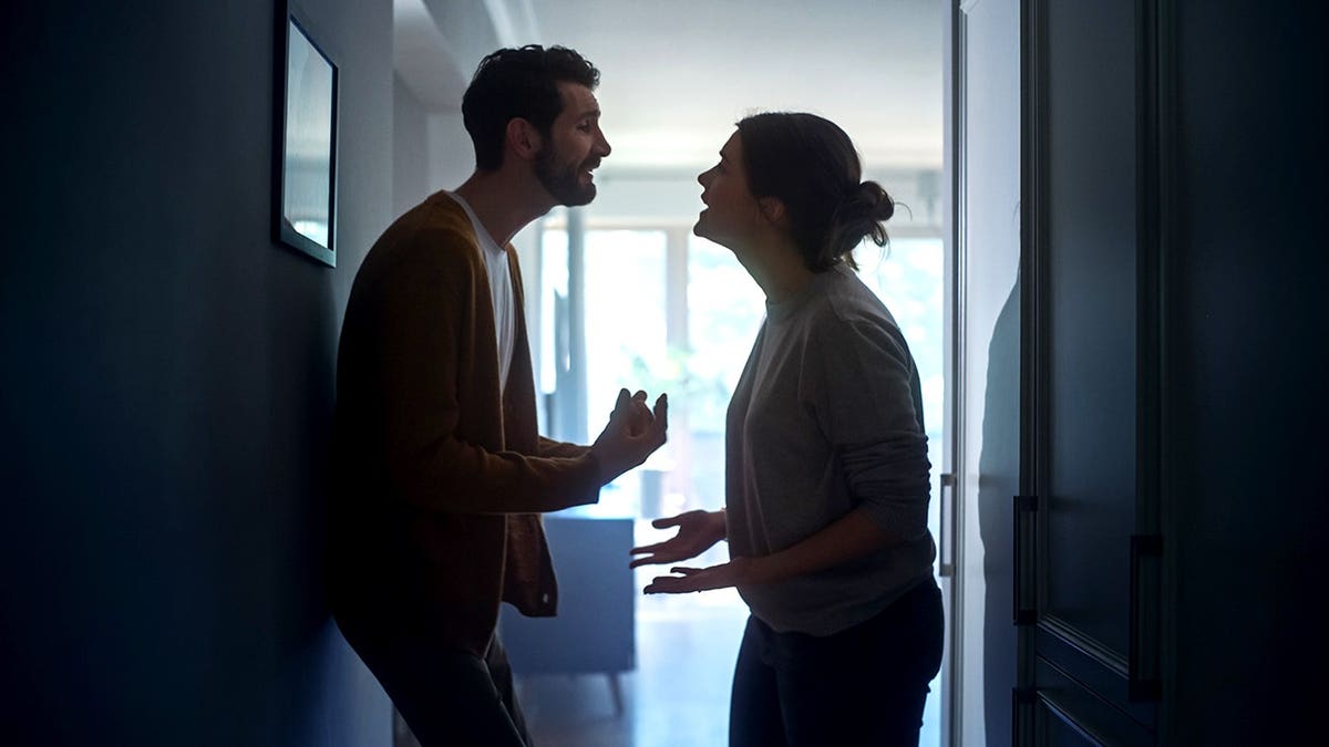 A young woman and man arguing in a dark apartment hallway