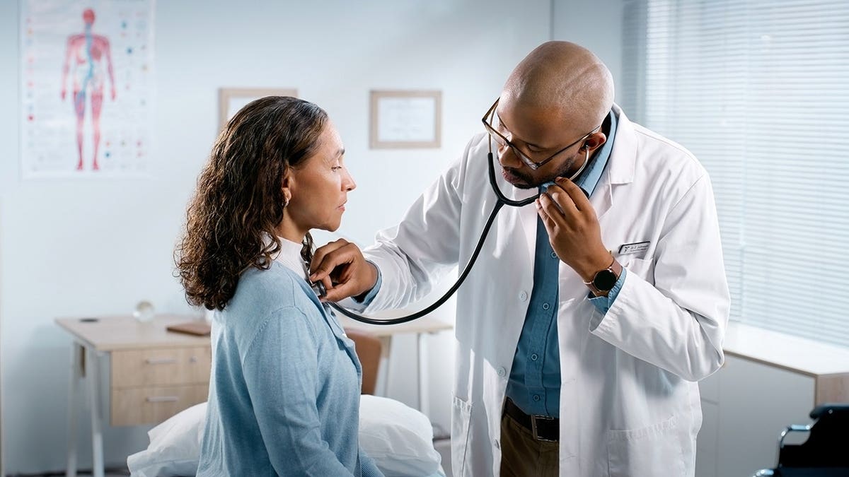 Woman doctor using stethoscope to examine man's chest in clinic
