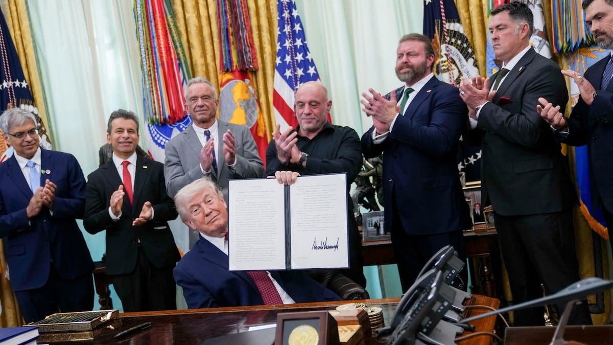 President Donald Trump holding a signed executive order in the Oval Office