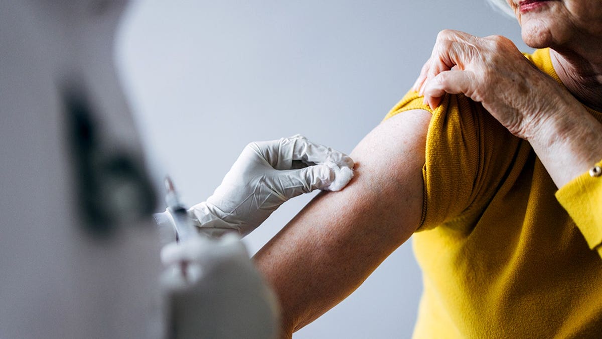 Healthcare professional administering vaccination to elderly woman seated