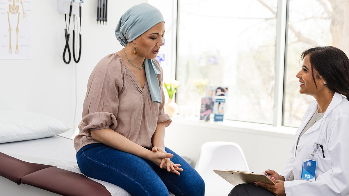 Female cancer patient sitting on examination table with female doctor in medical office