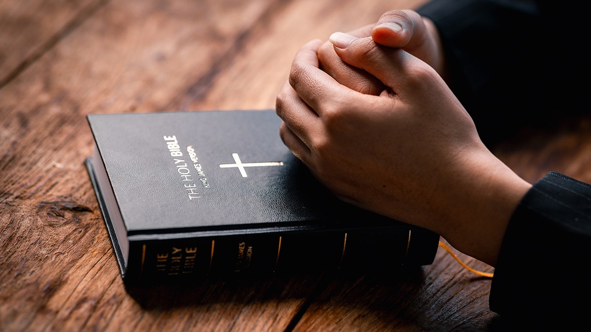 Woman's hands folded in prayer on a Holy Bible inside a church.