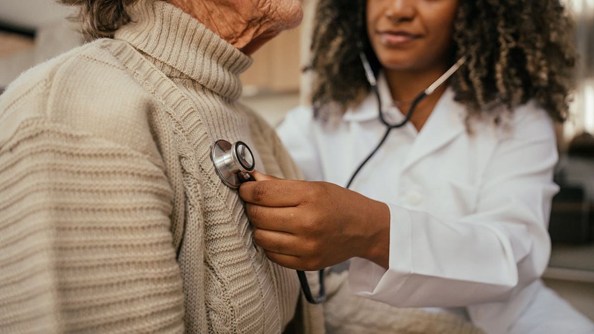 Healthcare professional listens to elderly woman’s heart with stethoscope at home