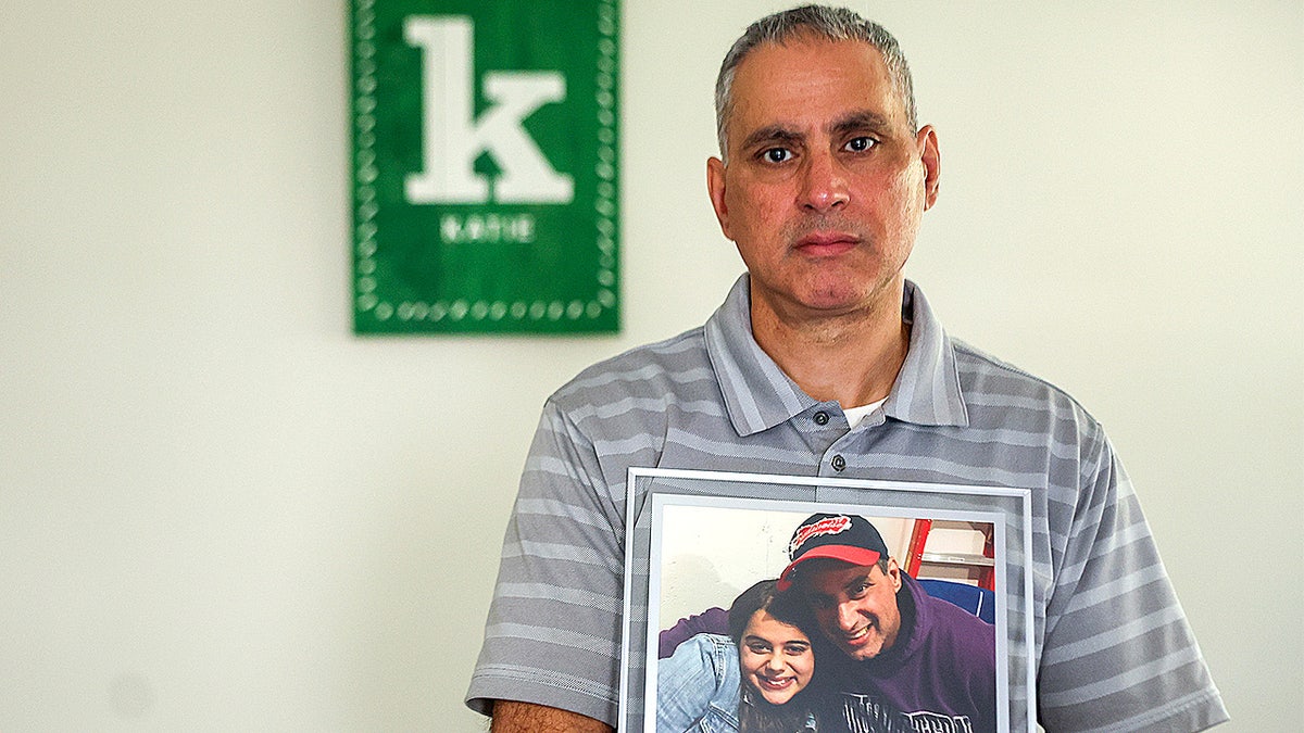 Joe Abraham holding a photograph of himself with his daughter Katie Abraham at home