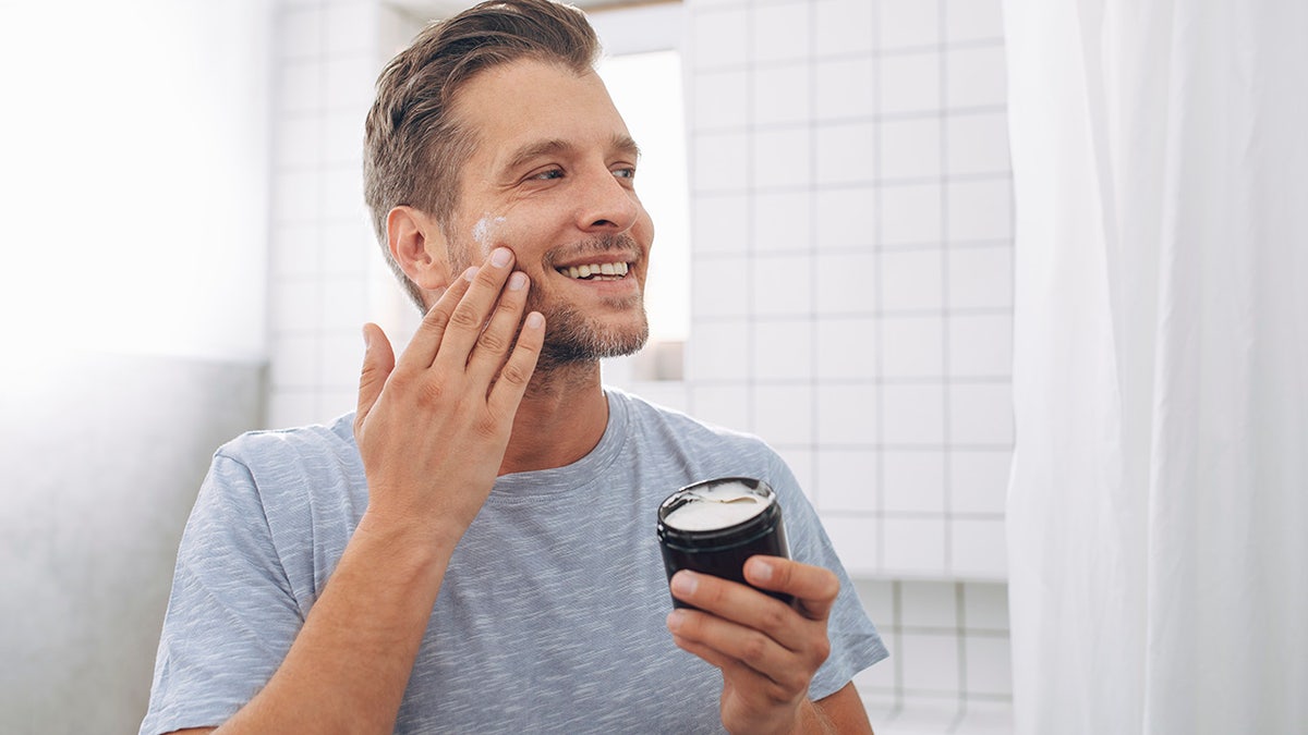 young man applying aftershave moisturizer in bathroom mirror