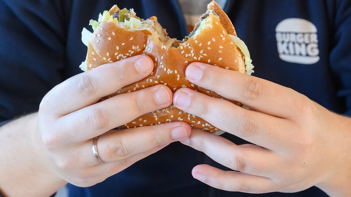 Man eating a Whopper, seen up close and wearing Burger King shirt