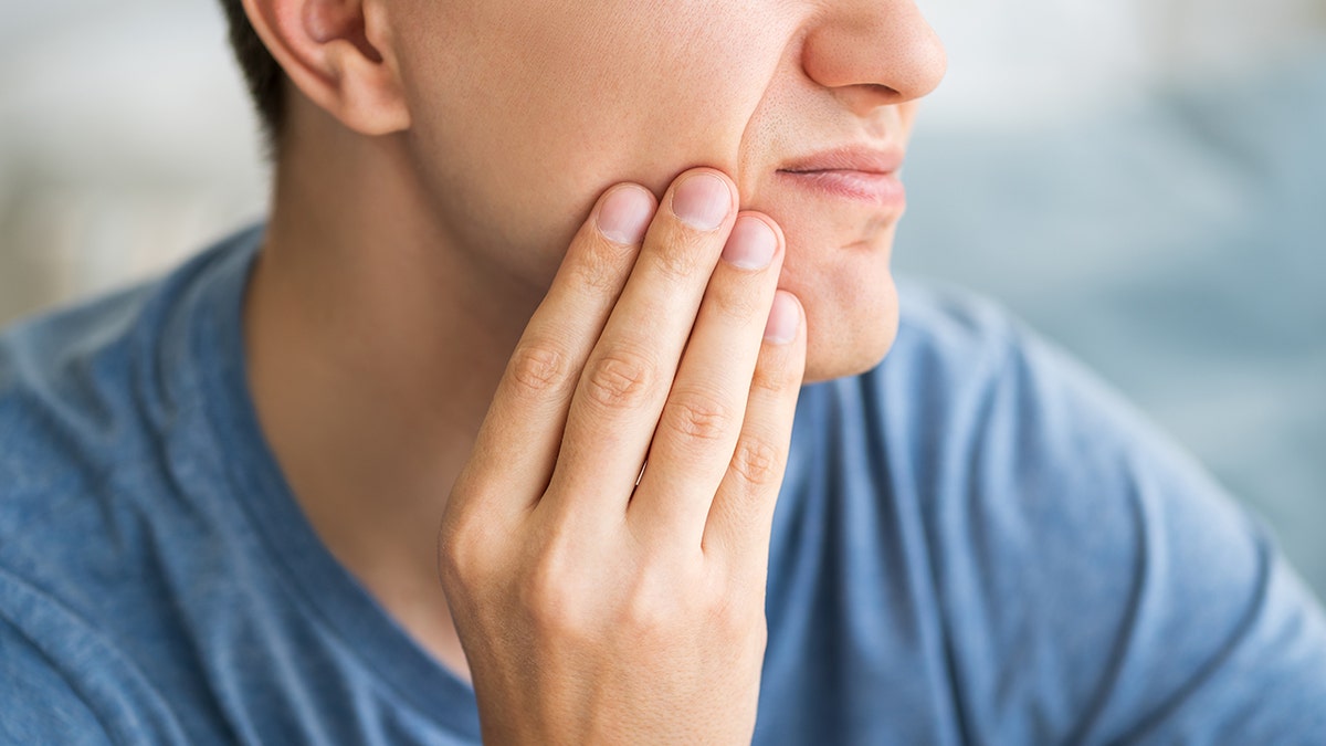 man holds his jaw in pain