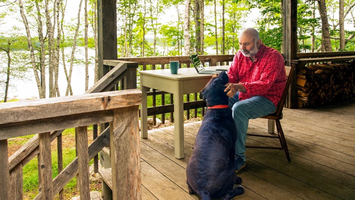 A mature man playing with his dog while taking a break from working on a computer.