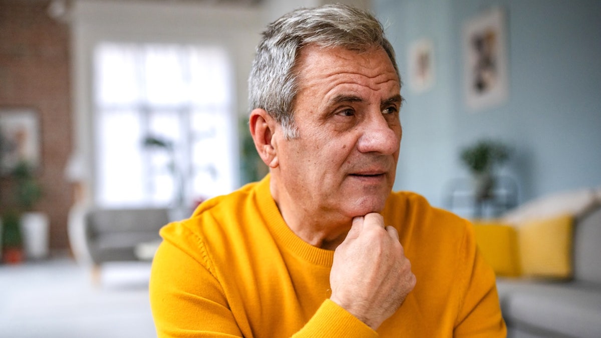 Worried older man sitting indoors with hands clasped