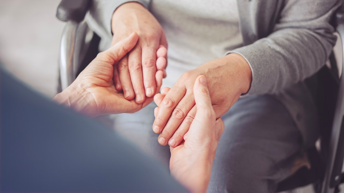 Young carer holding hands of elderly woman with Parkinson's disease