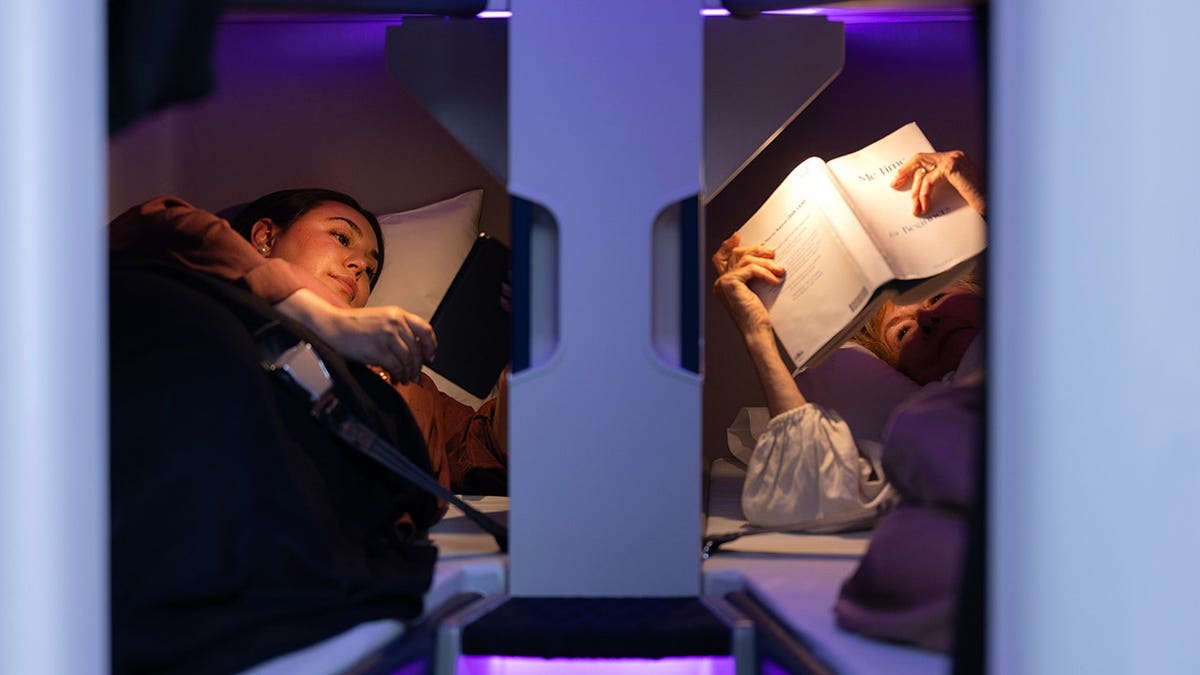 Passengers relaxing in Air New Zealand Economy Skynest pods, reading and resting in lie-flat sleeping spaces on long-haul flight.