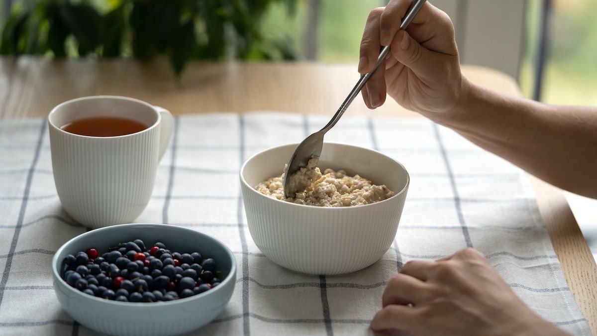 Woman eating oatmeal porridge with summer berries at a table